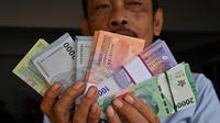 Seorang pria menunjukkan uang kertas Rupiah yang baru, yang akan diberikan kepada anggota keluarganya saat perayaan Idul Fitri, di Jakarta pada 28 Maret 2024. (Adek BERRY/AFP)