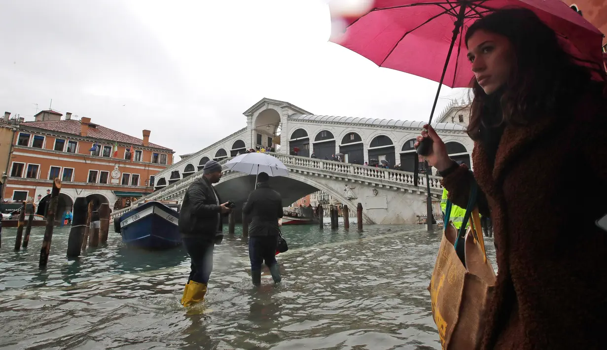 Warga berjalan dekat Jembatan Rialto saat gelombang pasang menerjang  di Venesia, Italia, Selasa (12/11/2019). Venesia dilanda banjir akibat gelombang pasang setinggi 127 cm. (AP Photo/Luca Bruno)