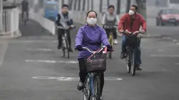 Warga mengendarai sepeda dengan memakai masker pada hari yang tercemar polusi udara di Beijing, China (2/4). (AFP Photo/Fred Dufour)