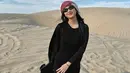 Saat di gurun pasir, Azizah tampil mengenakan dress hitam panjang yang dipadukan outer panjang warna serasi.  [@azizahsalsha_]