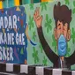 Seorang perempuan melewati mural yang mengajak orang untuk memakai masker di tengah pandemi Covid-19 di Surabaya, Minggu (25/10/2020). Mural di sepanjang dinding itu sebagai sarana imbauan kepada masyarakat untuk menerapkan protokol kesehatan pencegahan penularan COVID-19. (Juni Kriswanto/AFP)