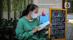 Warga membaca buku dekat perpustakaan bersama Bookhive Jakarta di kawasan Taman Situ Lembang, Jakarta, Selasa (27/4/2021). Warga bisa meminjam dan menyumbang buku pada rak terbuka Bookhive Jakarta. (Liputan6.com/Faizal Fanani)