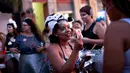 Seorang wanita membagikan stiker saat merayakan karnaval "Maria vem com as outras" di Rio de Janeiro, Brasil (3/2). Karnaval ini digelar agar mendorong wanita di Brasil melaporkan pelecehan jika terjadi pada mereka. (AP Photo / Silvia Izquierdo)