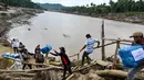 Salah satunya dengan melintasi tumpukan puing kayu untuk naik ke bagian jembatan yang masih utuh dan kokoh untuk dilewati. Tampak dalam foto, warga memindahkan bantuan logistik dengan melintasi sungai di jembatan yang baru dibangun yang menghubungkan Aceh dan Provinsi Sumatera Utara setelah jembatan tersebut hancur akibat banjir bandang di Sungai Peusangan, Bireuen, Provinsi Aceh, Selasa 9 Desember 2025. (CHAIDEER MAHYUDDIN/AFP)