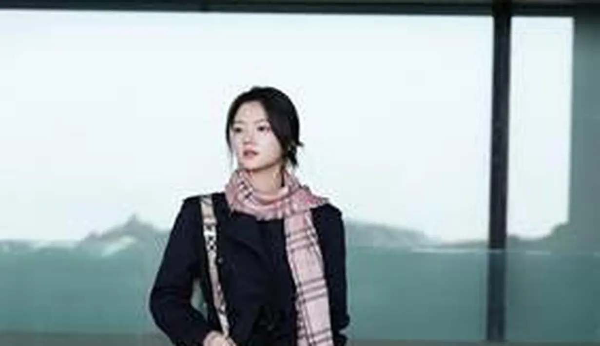 Mantel trench Waterloo berwarna biru tua, kaos oblong bermotif kotak-kotak hitam, celana joging, dan sepatu bot kulit, ditambah syal bermotif kotak-kotak EKD, tas ember B Clip putih, dan gantungan kunci beruang Thomas.