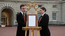 Pelayan kerajaan Stephen Kelly dan Sarah Thompson membawa papan pengumuman kelahiran anak pertama Pangeran Harry dan Meghan Markle di London, Inggris, Senin (6/5/2019). Dalam tradisi kerajaan, setiap kelahiran bayi akan diumumkan di depan Istana Buckhingham. (Yui Mok/Pool Photo via AP)