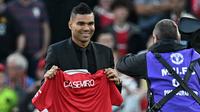 Casemiro yang berpakaian serba hitam, mulai dari jas sampai kemeja yang dikenakannya, berjalan menuju tengah lapangan. Di sana, ia memamerkan jersey barunya yang masih belum ada nomor punggungnya itu. (AFP/Paul Ellis)