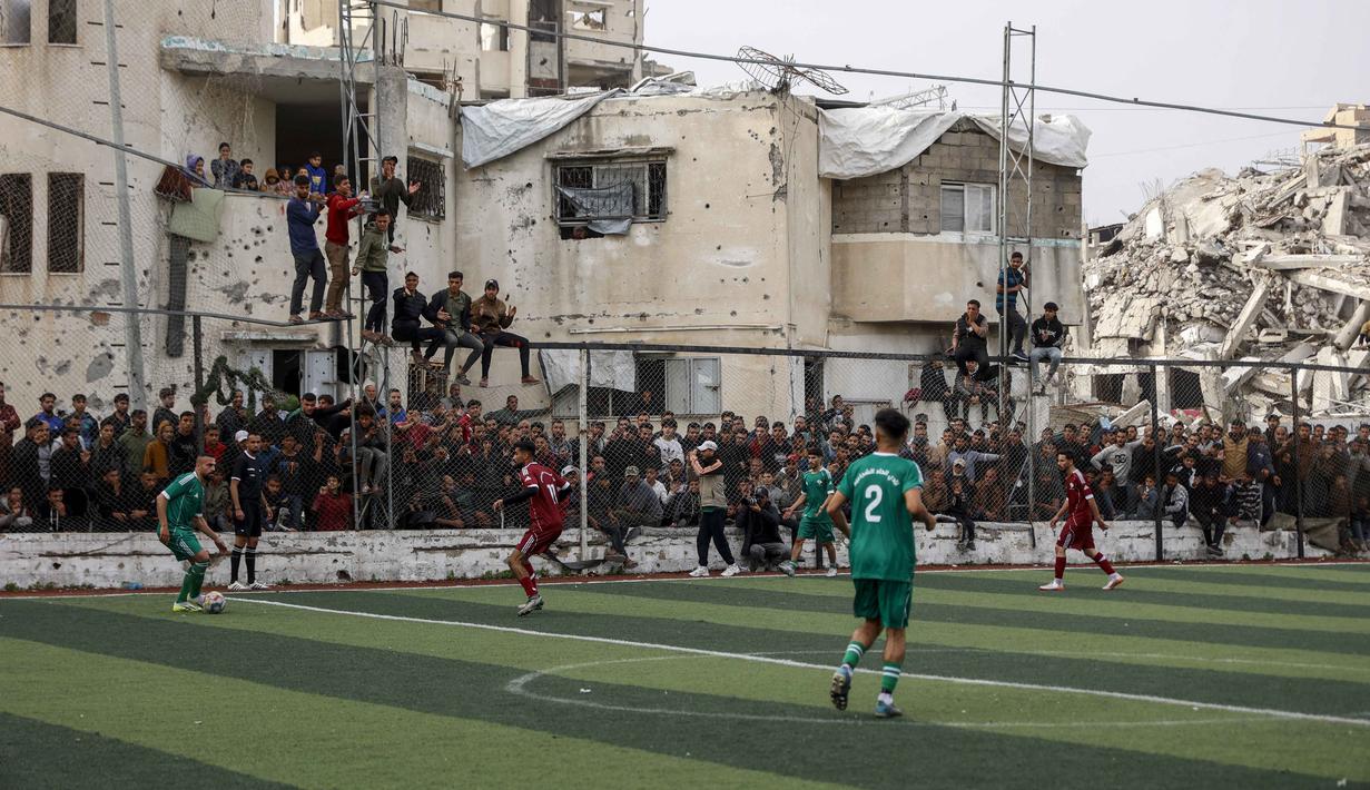 Seketika, aura kehidupan kembali bergelora melupakan luka perang yang masih terasa. Tampak dalam foto, warga Palestina menyaksikan pertandingan sepak bola lima lawan lima di tengah reruntuhan bangunan yang hancur di Kota Gaza pada Senin 9 Februari 2026. (Omar AL-QATTAA/AFP)