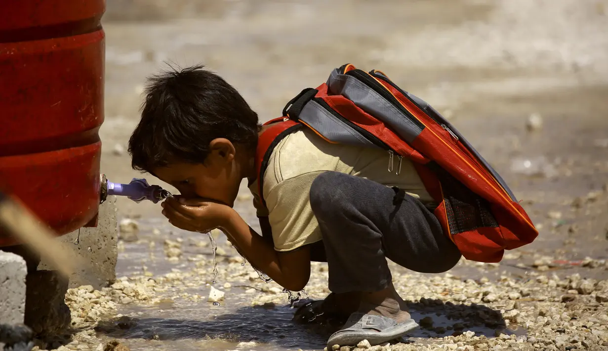 Seorang anak meminum air dari wadah penampungan sebelum berangkat ke sekolah di sebuah kamp di Ain Issa, Suriah (22/8). (AFP Photo/Delil souleiman)
