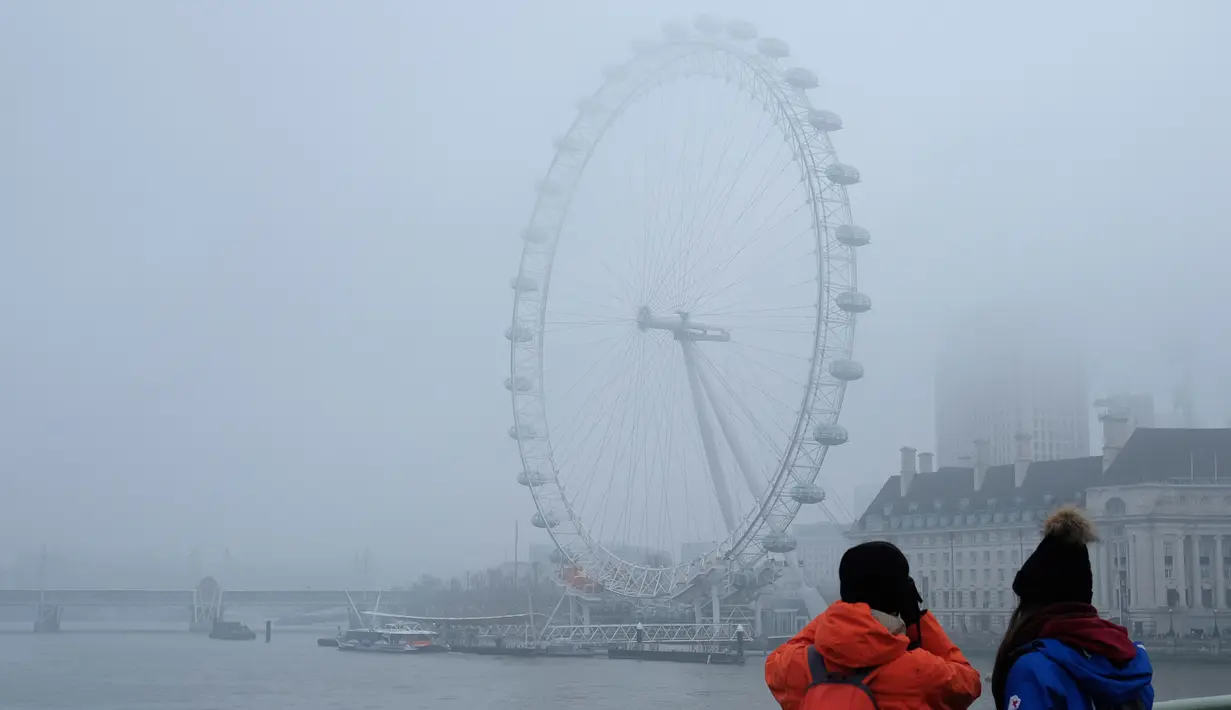 Wisatawan mengambil gambar The London Eye saat diselimuti kabut Inggris, Senin, (23/1). Aktifitas warga menjadi terganggu karena terbatasnya jarak pandang (AP Photo / Alastair Grant)