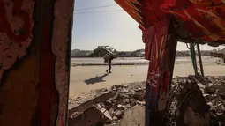 Seruan itu disampaikan Menteri Luar Negeri Mesir, Badr Abdelatty, Sabtu (6/12/2025). Tampak dalam foto, seorang pria membawa kardus berjalan melewati bangunan hancur yang dipenuhi mural di kamp pengungsi Maghazi di luar Deir al-Balah pada Senin 8 Desember 2025. (EYAD BABA/AFP)