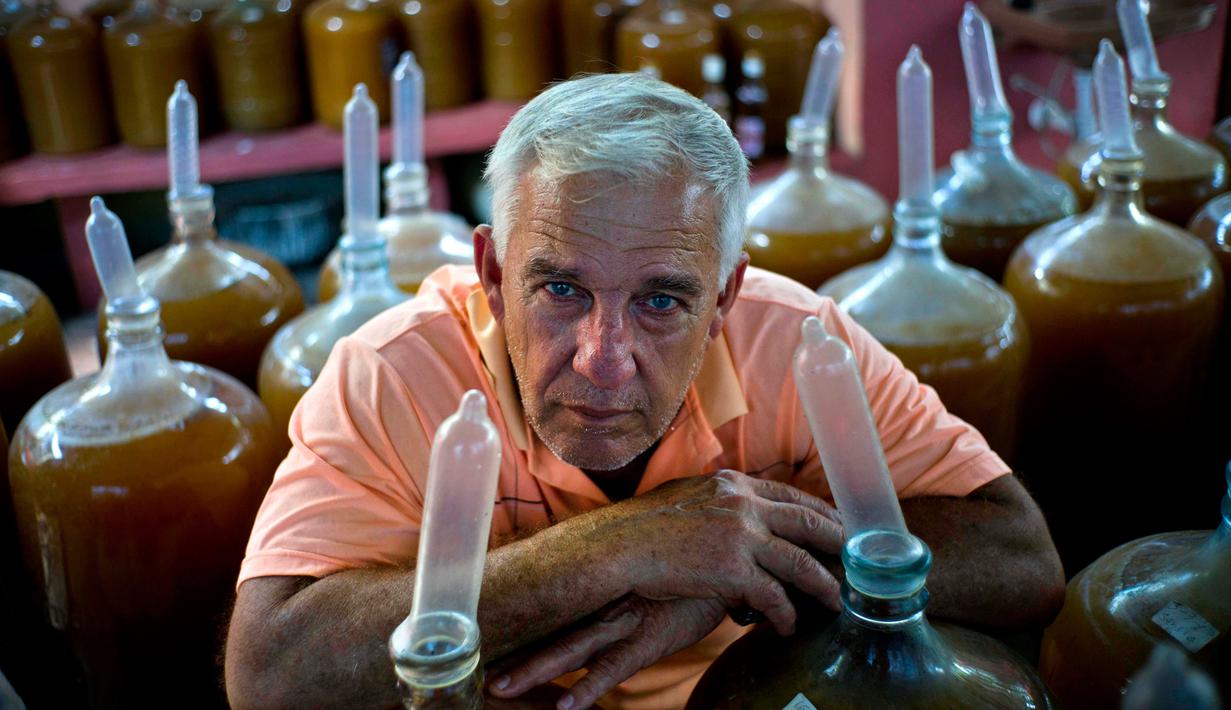 Pembuat minuman wine, Orestes Estevez berpose di dekat kendi berisikan anggur buatannya di Havana, Kuba, Kamis (30/3). Orestes menggunakan kondom sebagai penutup kendi dari anggur racikannya. (AP Photo)