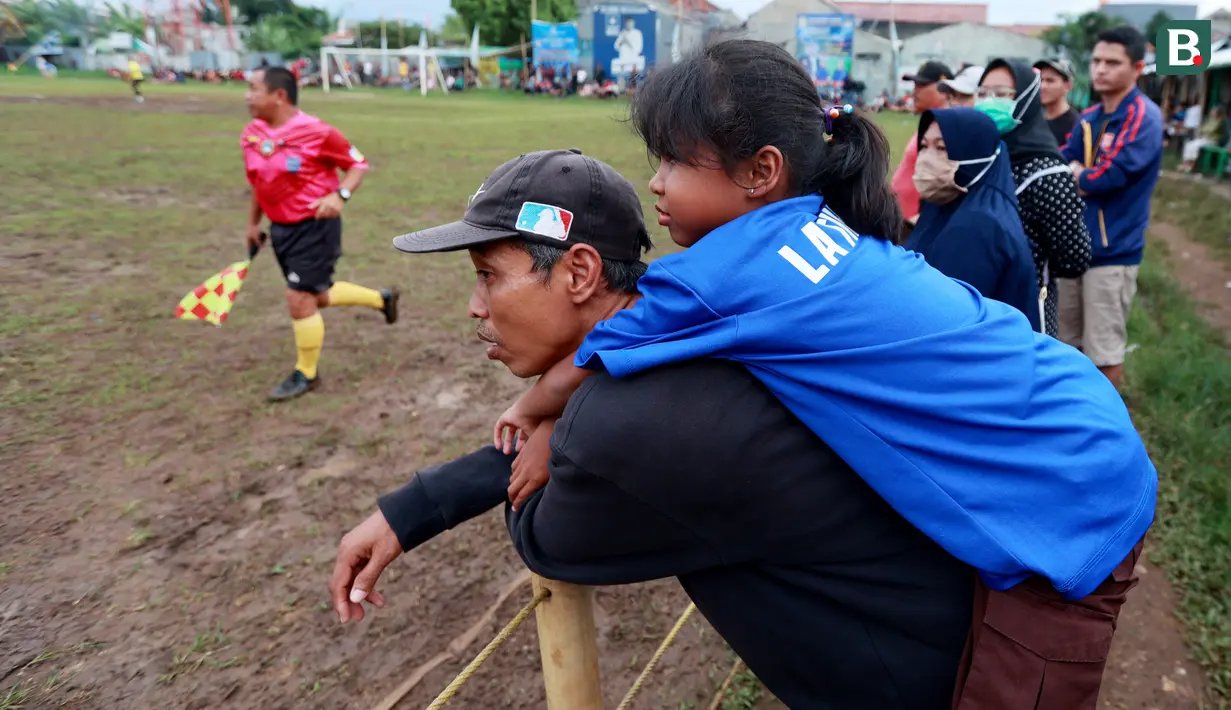 Seorang anak digendong bapaknya tampak asik menyaksikan pertandingan antara Ad-Sya FC melawan Dejan FC di Lapangan Latus Jaya, Kedaung, Pamulang, Minggu (12/3/2023). (Bola.com/M Iqbal Ichsan)