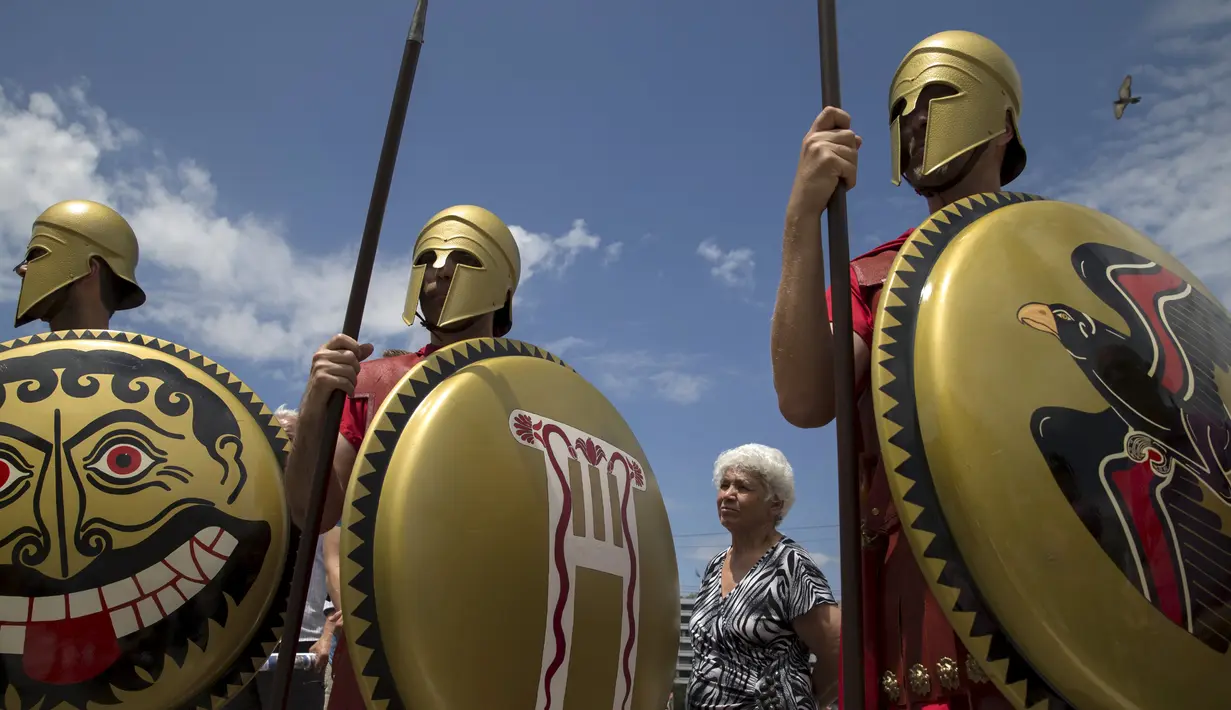 Seorang wanita berdiri di antara Para pria menggunakan pakaian tentara Yunani kuno membawa tombak dan tameng di sekitar Syntagma Square. Athena, Yunani (21/6/2015). (REUTERS/Marko Djurica)