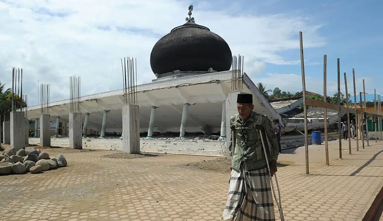 Seorang pria berjalan melewati sebuah masjid yang rusak usai gempa di Pidie Jaya, Aceh, Rabu (7/11). Selain meruntuhkan bangunan, gempa bumi berkuatan 6,4 SR ini telah menelan banyak korban jiwa. (AFP PHOTO / Chaideer Mahyuddin)