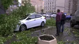 Dua orang pria berada di dekat mobil yang tertimpa pohon di Moskow, Rusia (29/5). Badai berkecepatan 110 km per jam diserta hujan es itu menyebabkan 11 orang tewas dan 69 orang terluka. (AP Photo)