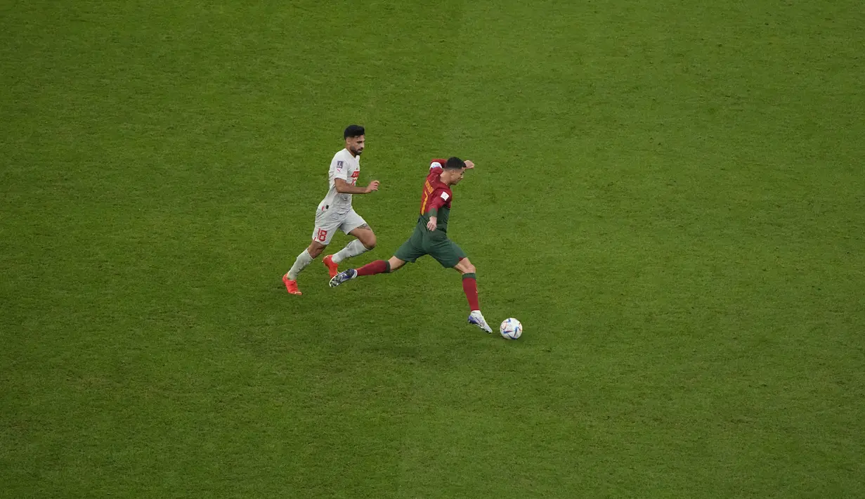 Penyerang Portugal Cristiano Ronaldo berlari dengan bola di sebelah bek Swiss Eray Comert dalam laga 16 besar Piala Dunia 2022 di Stadion Lusail Iconic, Rabu (7/12/2022) dini hari WIB. Pemain bernomor punggung 7 itu memulai laga Portugal vs Swiss dari bangku cadangan. (AP Photo/Ariel Schalit)