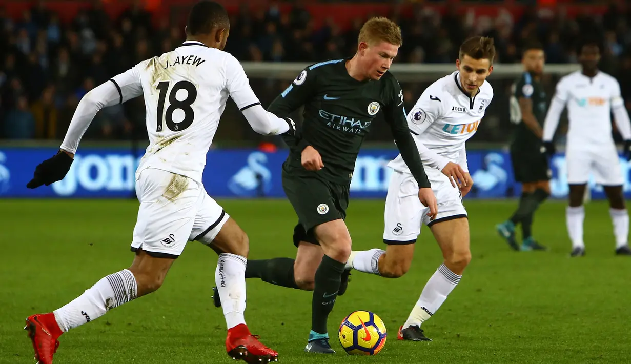 Bek Manchester City, Kevin De Bruyne menggiring bola dengan kawalan pemain Swansea City pada lanjutan Premier League di Liberty Stadium, Rabu (13/12). Man City mencatatkan rekor 15 kemenangan berturut-turut usai menang 4-0. (GEOFF CADDICK / AFP)