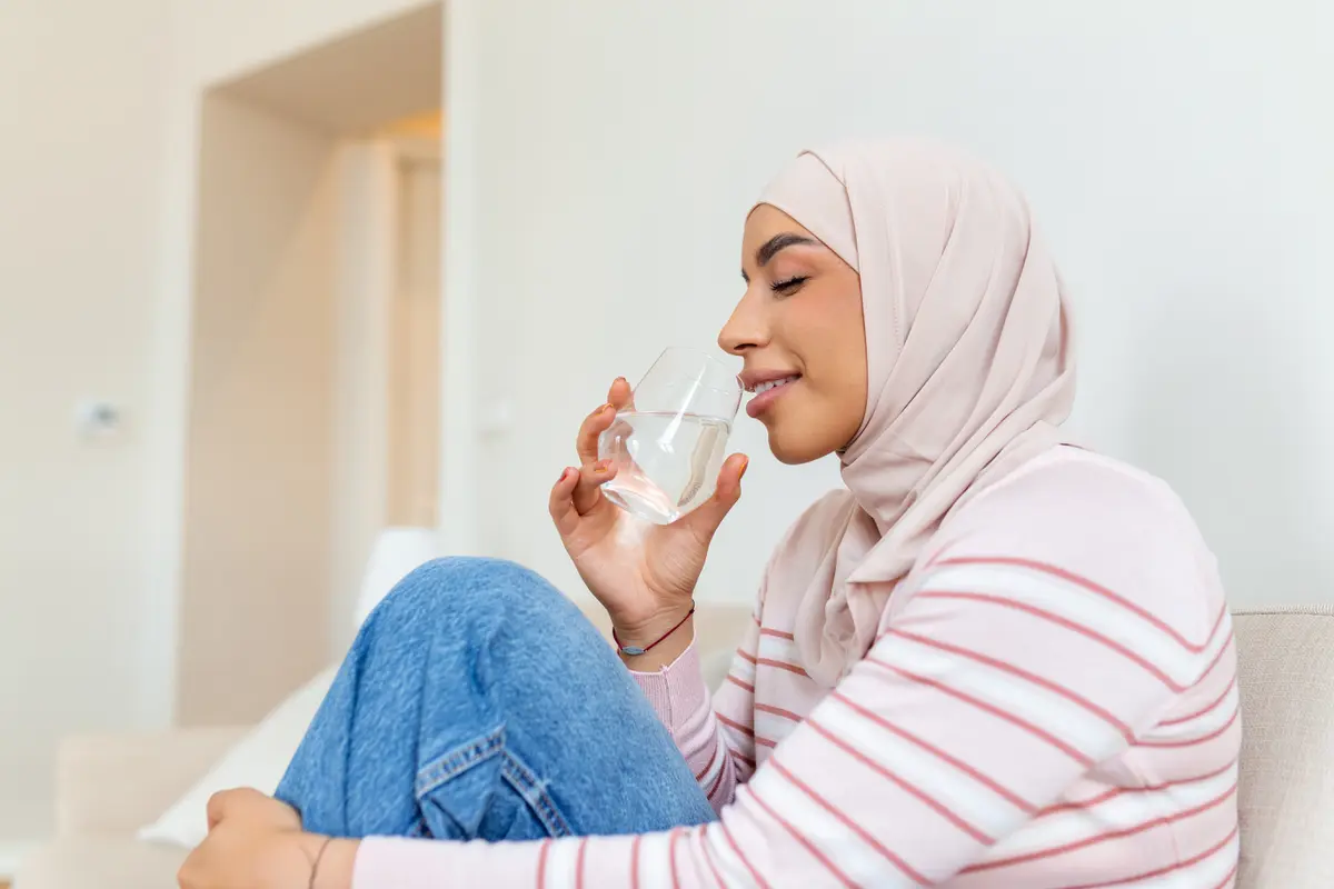 Seorang wanita muslimah mengenakan jilbab pink sedang minum air putih (Foto Dok: Freepik/ stefamerpik)