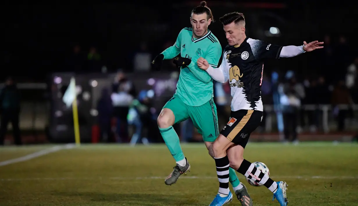 Winger Real Madrid, Gareth Bale berebut bola dengan bek Unionistas de Salamanca, Juan Gongora pada pertandingan babak ke-32 besar Copa del Rey 2019-2020 di Pistas del Helmantico, Rabu (22/1/2020). Madrid harus berjuang keras untuk menang 3-1 atas tim divisi tiga, Unionistas. (JAVIER SORIANO/AFP)