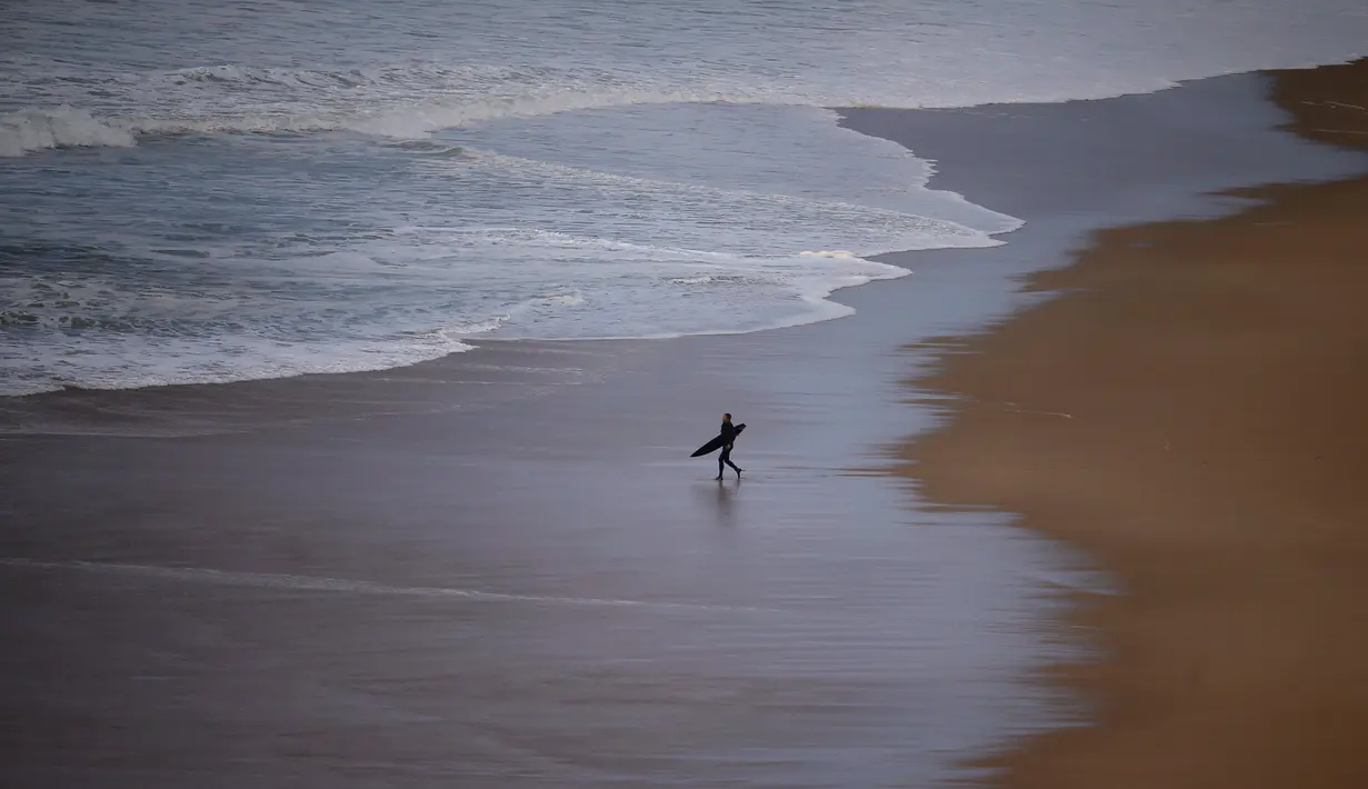 Seorang peselancar berjalan di pinggir pantai menunggu ombak besar saat berselancar di Praia do Norte di Nazare, Portugal (19/11). (Reuters/Rafael Marchante)