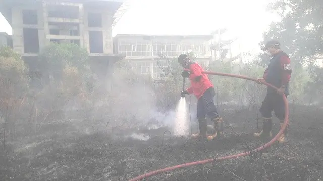 Petugas pemadam kebakaran Kota Pekanbaru menyemportkan air di lahan terbakar dekat pemukiman warga.