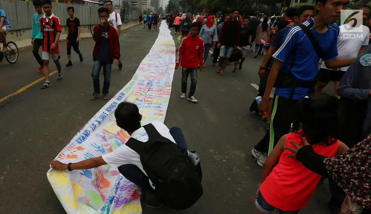Warga membentangkan spanduk bekas Cap tangan anak-anak Indonesia, di Kawasan Car Free Day, Jakarta (24/9). Spanduk sepanjang satu kilometer tersebut untuk menunjukkan dukungan kepada Etnis minoritas Rohingya di Myanmar. (Liputan6.com/Johan Tallo)