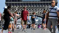 Turis berjalan di depan Menara Eiffel, Paris, Kamis (2/8). Dua hari terakhir atau sejak Rabu (1/8), karyawan menara yang menjulang setinggi 324 meter ini mogok. (AFP PHOTO/GERARD JULIEN)