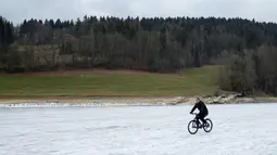 Seorang pria bersepeda di atas sungai Doubs yang membeku di perbatasan Perancis Les Brenets, Swiss, Senin (2/1). Sungai ini menjadi objek wisata es yang diminati warga. (REUTERS/Denis Balibouse)