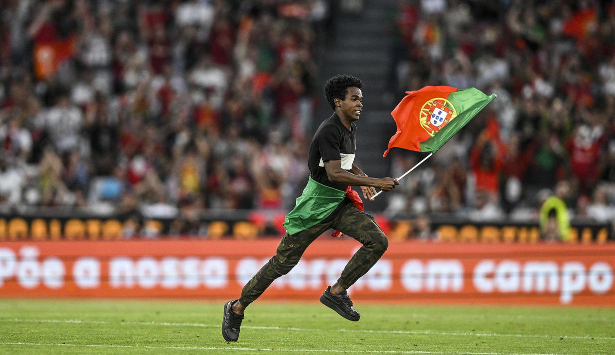 Seorang penyusup lapangan berlari sambil mengibarkan bendera Portugal di tengah laga Grup J Kualifikasi Euro 2024 antara Timnas Portugal menghadapi Bosnia Herzegovina di Luz Stadum, Lisbon, Portugal, Minggu (18/6/2023) dini hari WIB. (AFP/Patricia De Melo Moreira)