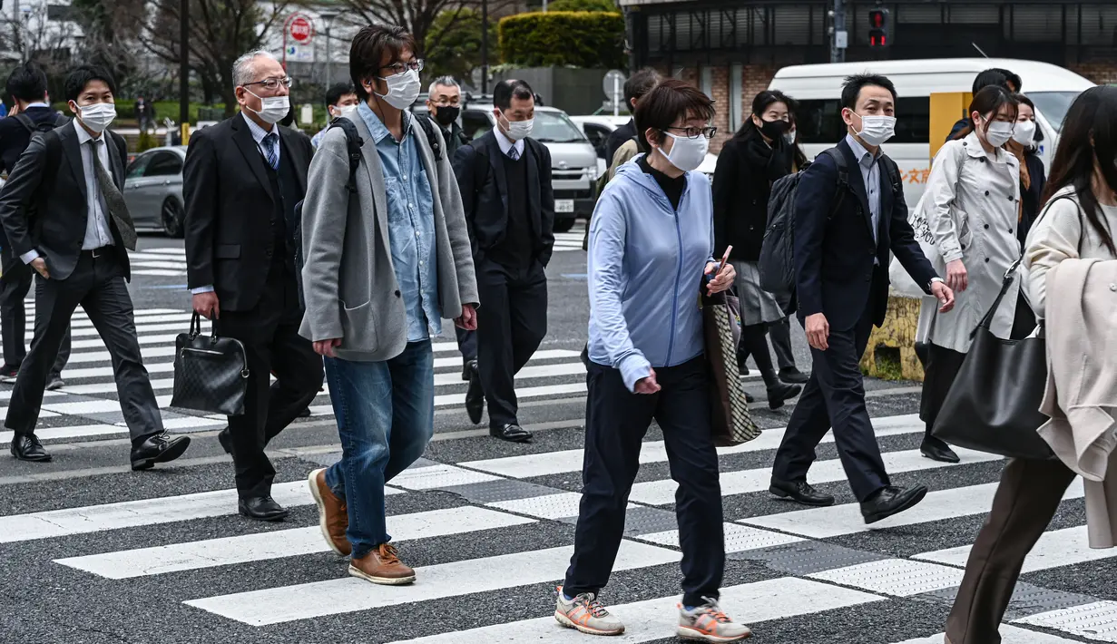 Komuter melintasi jalan di pusat kota Tokyo pada hari pertama pemerintah Jepang mencabut ketentuan wajib mengenakan masker, Senin (13/3/2023). Maskapai penerbangan, kereta api, bus, dan transportasi umum lainnya tidak akan lagi meminta pelancong untuk memakainya. (Photo by Kazuhiro NOGI / AFP)