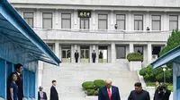 Presiden Amerika Serikat, Donald Trump bersama Pemimpin Korea Utara, Kim Jong-un berjalan menuju garis yang memisahkan kedua wilayah Korea di zona demiliterisasi Korea (DMZ), Desa Panmunjom pada Minggu (30/6/2019).  (Brendan Smialowski/AFP)