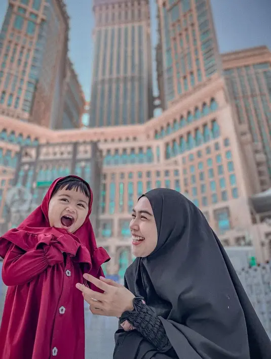 Ria Ricis berpose bersama Moana saat Umroh. Ricis yang memilih tampilan serba hitam tampak berpose tertawa menggemaskan di samping sang putri Moana, yang memilih tampilan serba merah. [Foto: Instagram/riaricis1795]