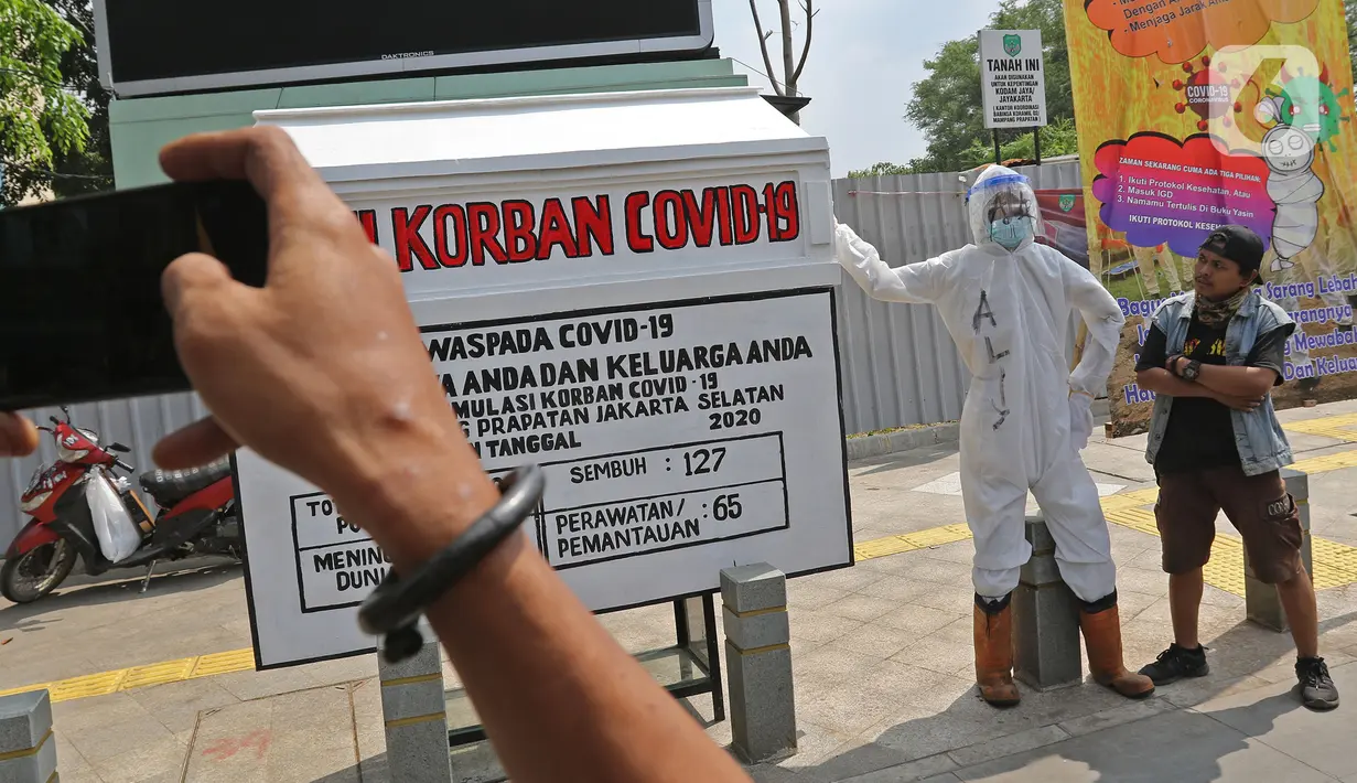 Seorang pria berpose di depan seni instalasi yang menggambarkan tenaga medis memegang peti jenazah korban COVID-19 di Kemang 1, Jakarta Selatan, Minggu (16/8/2020). Seni instalasi itu dipajang guna memberi peringatan kepada warga untuk tetap waspada terhadap COVID-19. (Liputan6.com/Herman Zakharia)