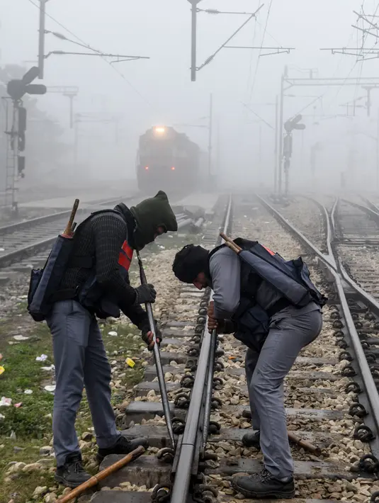 Pekerja memperbaiki jalur kereta api di tengah kabut tebal selama hari yang dingin di stasiun kereta api di Amritsar, India (30/12/2019). (AFP/Narinder Nanu)