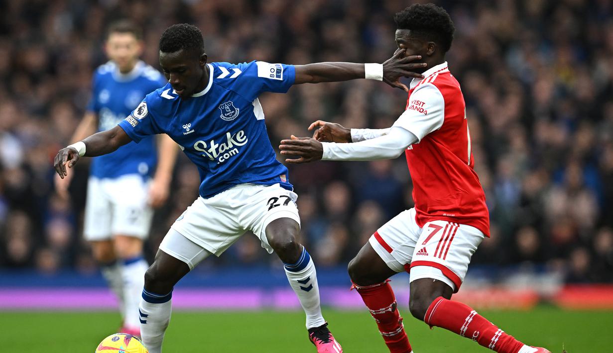 Gelandang Everton, Idrissa Gueye (kiri) menguasai bola dibayangi gelandang Arsenal, Bukayo Saka pada laga Liga Inggris 2022/2023 di Goodison Park, Liverpool (4/2/2023). Idrissa Gueye kembali ke Everton setelah tiga musim membela PSG. Karena telah mengenakan nomor punggung 27 bersama PSG, ia kembali meneruskan menggunakan nomor tersebut di periode keduanya bersama Everton. (AFP/Paul Ellis)