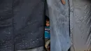 Pemerintah kota Jabalia melaporkan, sekitar 90 persen peralatan operasional untuk membersihkan puing-puing dan memulihkan infrastruktur dasar telah lumpuh atau hancur. Tampak dalam foto, seorang anak mengintip dari balik terpal di kamp pengungsian di Jabalia, di bagian utara Jalur Gaza, Minggu 7 Desember 2025. (AP Photo/Jehad Alshrafi)