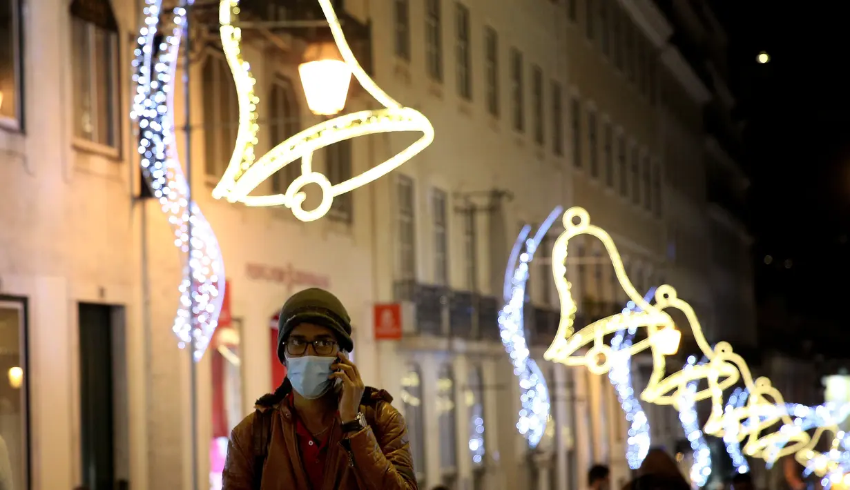 Seorang pria yang mengenakan masker berjalan di bawah lampu-lampu Natal dan Tahun Baru pada masa pandemi COVID-19 di Kota Lisbon, Portugal, 17 Desember 2020. Portugal akan memberlakukan aturan jam malam dalam upaya mengurangi penyebaran COVID-19. (Xinhua/Pedro Fiuza)