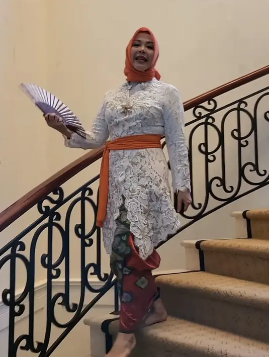 Istri Menteri Pariwisata, Nur Asia mengenakan kebaya putih panjang brokat dipadukan kain Bali. Lengkap mengenakan obi oranye yang serasi dengan kerudungnya. Instagram/@nurasiauno