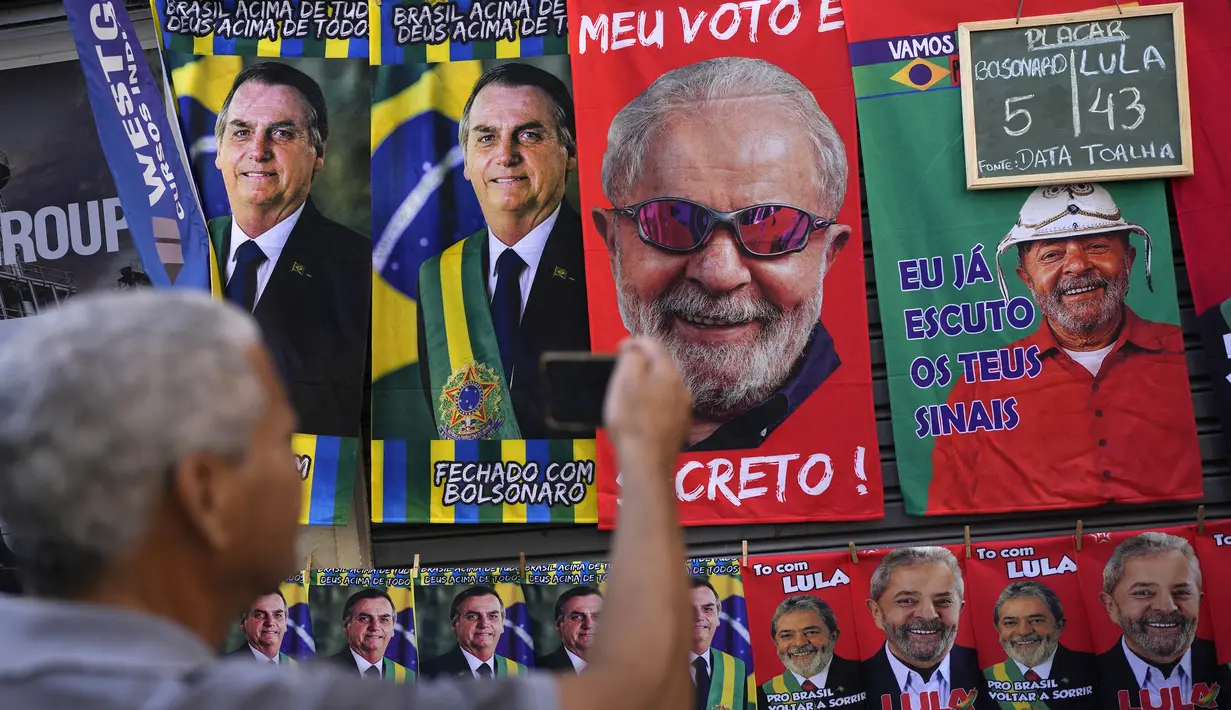 Seorang pria mengambil foto handuk bergambar Presiden Brasil Jair Bolsonaro (kiri) dan mantan Presiden Brasil Luiz Inacio da Silva atau Lula yang digantung untuk dijual menjelang pemilihan umum presiden di Rio de Janeiro, Brasil, 27 Juli 2022. Persilangan ideologi kedua kandidat mencerminkan perpecahan yang melanda Brasil. (AP Photo/Silvia Izquierdo)