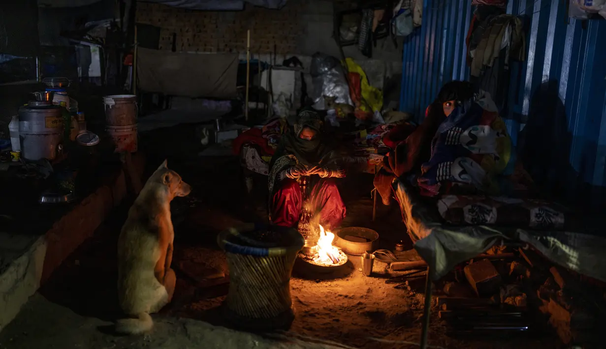 Sebuah keluarga tunawisma dan anjing mereka duduk di sekitar api unggun di luar tempat penampungan tunawisma pada malam yang dingin di New Delhi, Rabu, 28 Desember 2022. Angka resmi menunjukkan 195 tempat penampungan tunawisma di kota itu hanya dapat menampung sekitar 19.000 orang, menyisakan puluhan dari ribuan berjuang untuk tetap hangat. (AP Photo/Altaf Qadri)