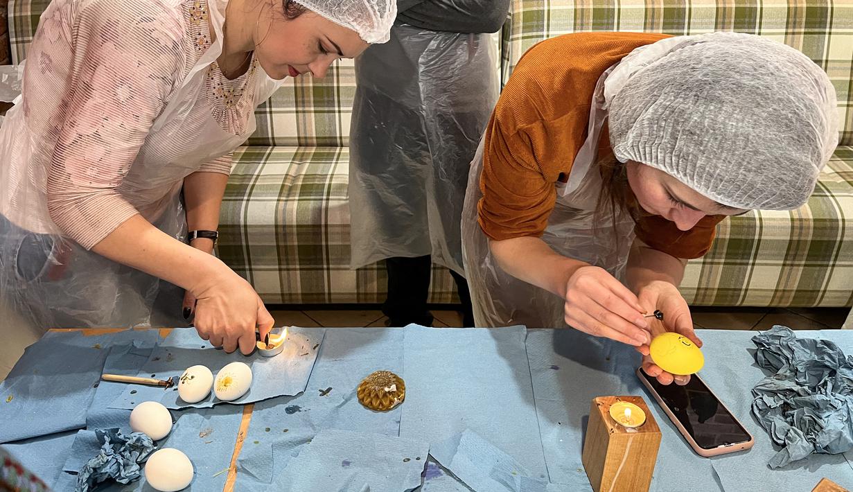 Wanita dan anak-anak Ukraina menghias telur Paskah untuk tentara dalam restoran Georgia di Lviv, Ukraina, 20 April 2022. Lebih dari selusin wanita dan anak-anak menghias telur rebus dan es roti Paskah tradisional dengan warna kuning dan biru, warna bendera Ukraina. (Alice HACKMAN/AFP)