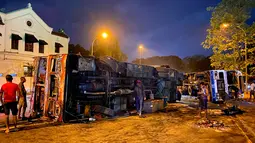 Orang-orang melihat bus hancur yang tergeletak di dekat kediaman resmi Perdana Menteri Sri Lanka Mahinda Rajapaksa, di Kolombo pada 9 Mei 2022. Puluhan bus yang digunakan oleh loyalis Rajapaksa untuk melakukan perjalanan ke Kolombo pada hari sebelumnya dibakar atau rusak di seluruh negeri. (ISHARA S. KODIKARA / AFP)