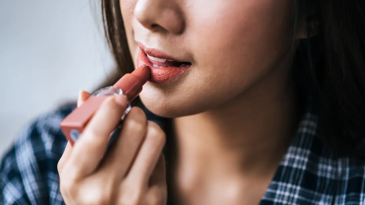 Seorang perempuan sedang mengaplikasikan lipstik di bibirnya (Foto Dok: Freepik/jcomp)