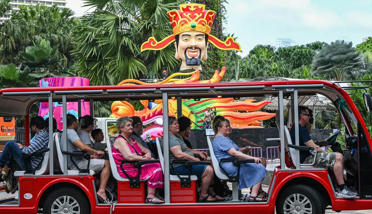 Para pengunjung duduk di dalam kendaraan yang melaju melewati struktur Dewa Keberuntungan yang dipasang sebagai persiapan menyambut Tahun Baru Imlek di sekitar jalur pengamatan hutan Supertrees di Gardens by the Bay, Singapura, pada tanggal 15 Januari 2024. (Roslan RAHMAN/AFP)