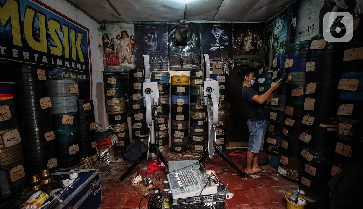 Adul (29) mencari film seluloid 35mm untuk pertunjukan layar tancap di gudang rumahnya di Jakarta, Rabu (28/4/2021). Sambil sesekali saat alat bisa digunakan mereka menggelar layar tancap untuk menghibur warga di lingkungan mereka saja. (Liputan6.com/Johan Tallo)