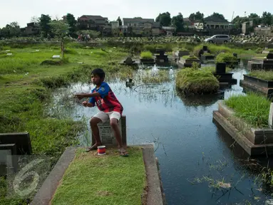 Seorang bocah bermain layang-layang diatas makam di Tempat Pemakaman Umum (TPU) Tanah Kusir, Jakarta, Selasa (25/4). (Liputan6.com/Gempur M. Surya)