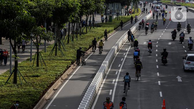 Para pesepeda (kanan) melintasi jalur kendaraan bermotor saat uji coba pembatas jalur sepeda permanen di kawasan Sudirman, Jakarta, Minggu (28/2/2021). Uji coba berlangsung selama tahap penyempurnaan jalur sepeda permanen yang ditargetkan rampung akhir Maret 2021. (Liputan6.com/Johan Tallo)