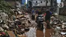 Pengendara sepeda motor melintas saat warga membersihkan sampah sisa banjir di Kebalen, Jakarta, Minggu (21/2/2021). Banjir yang terjadi kemarin karena curah hujan yang tinggi meninggalkan sampah di rumah warga. (Liputan6.com/Johan Tallo)