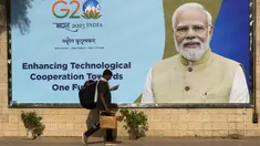 Seorang buruh migran memeriksa ponselnya saat ia berjalan melewati papan reklame bergambar Perdana Menteri India Narendra Modi, yang dipasang menjelang KTT negara-negara Kelompok 20 minggu ini di New Delhi, Senin, 4 September 2023. (AP Photo/Manish Swarup)